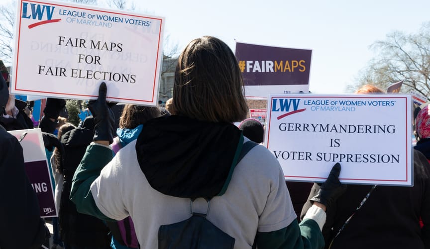 A protestor holds signs that say fair maps for fair elections and gerrymandering is voter suppression