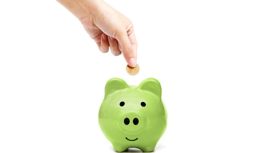 A hand putting a coin into a green piggy bank