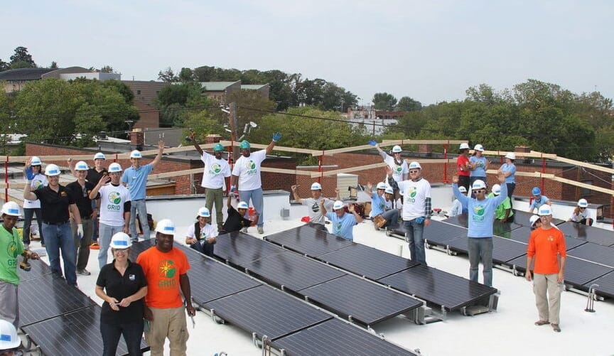 A group of people in hardhats cheering on a rooftop next to solar panels