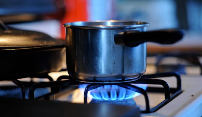A close-up of a saucepan on a gas stove burner with bluish flames underneath it