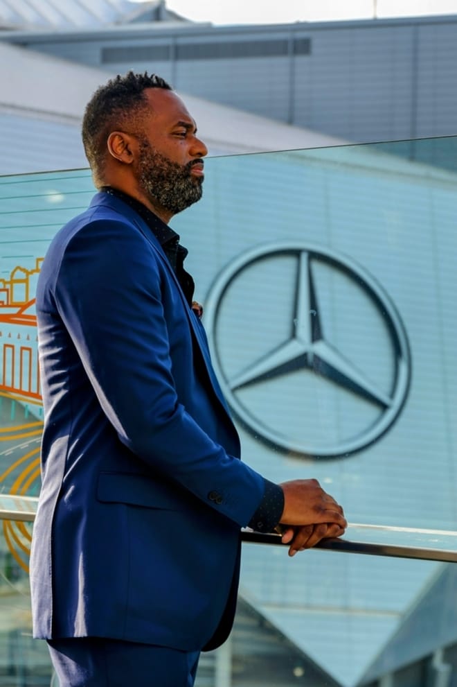 a Black man in a dark blue suit standing in profile