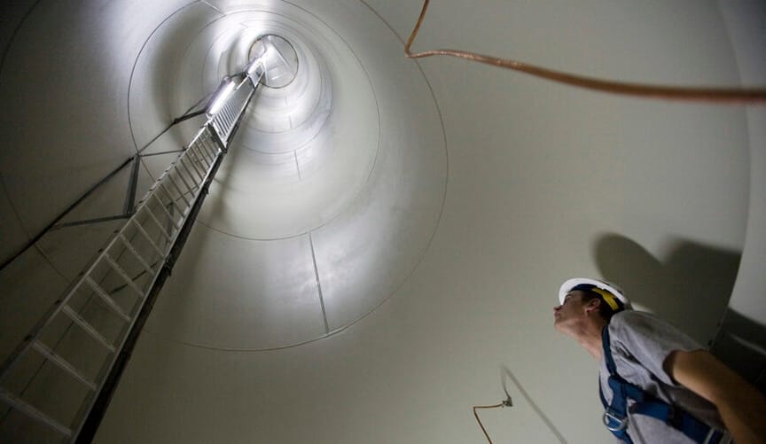 A repair technician looks up the large cylindrical interior of a wind turbine