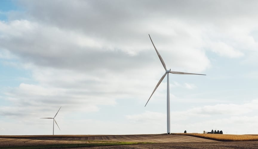 Two large white wind turbines in a field against a light blue sky with large wispy clouds