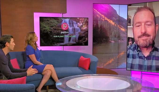 A male and a female TV host sit on a couch and talk to a man on video screen