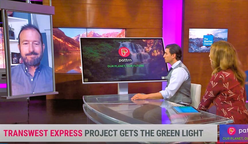 A man on a video screen chats with male and female TV hosts