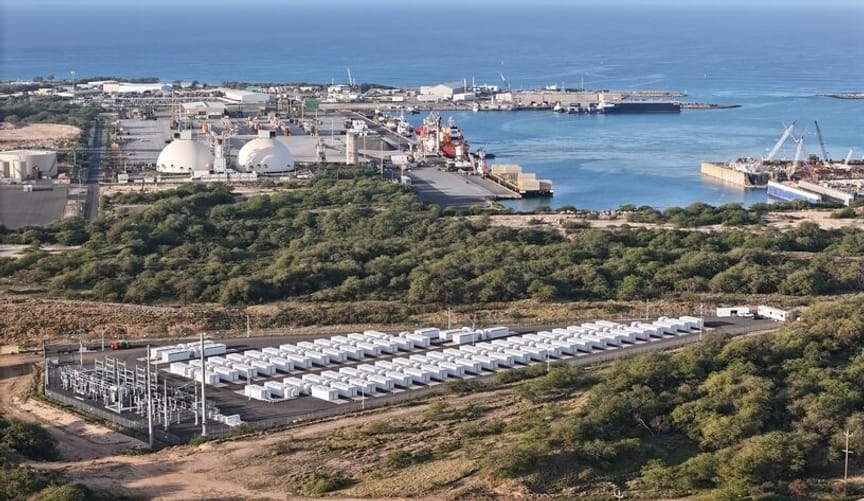 An aerial view of a large battery site comprising many white rectangular metal boxes next to the ocean