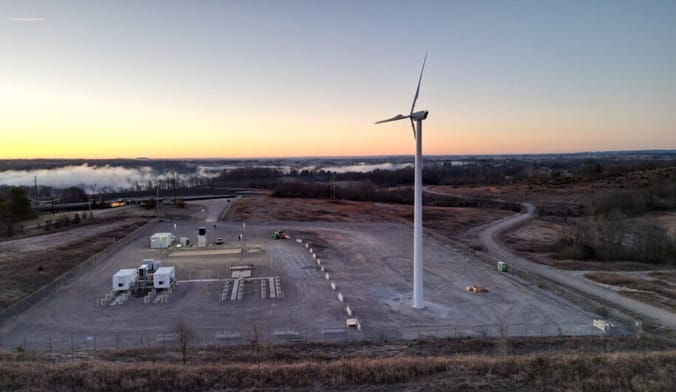 A lone white wind turbine sits motionless at an empty industrial site