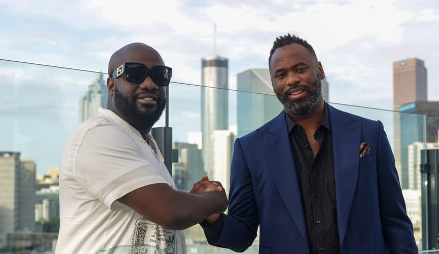 Two Black men clasp hands in front of a city skyline