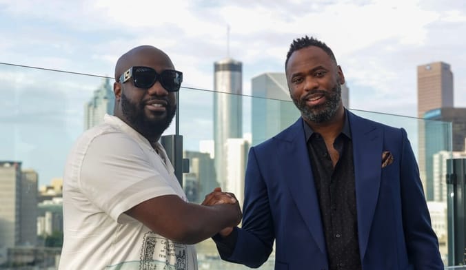 Two Black men clasp hands in front of a city skyline