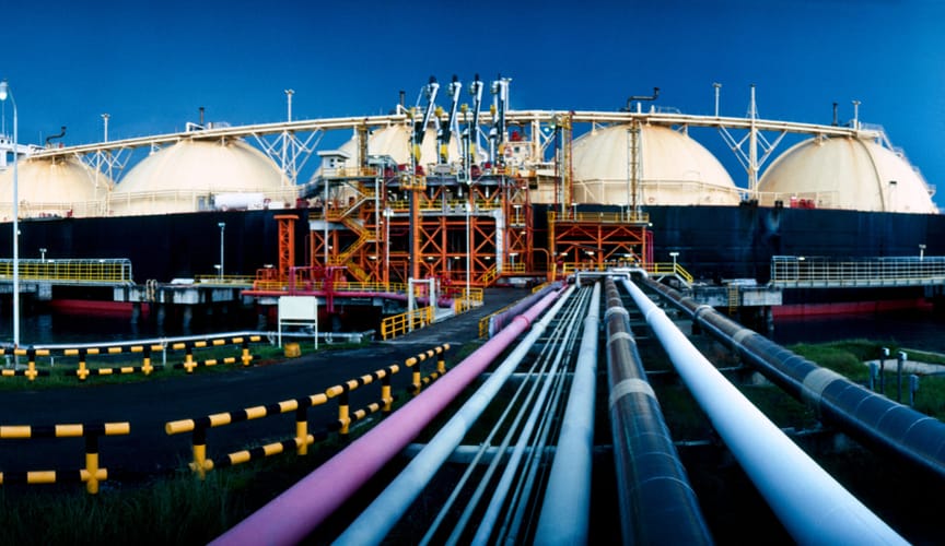A close-up shot of several long, multicolored pipelines connected to a large dark blue LNG tanker