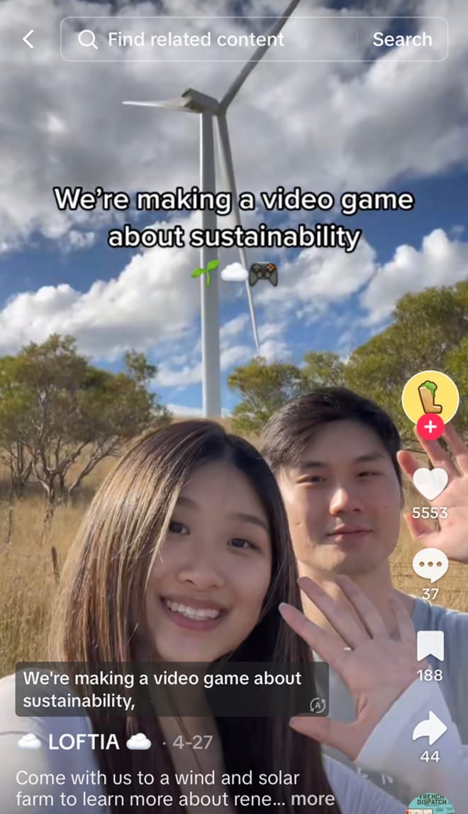 A woman with long dark hair and a man with short dark hair wave at the camera. Behind them is a large wind turbine.