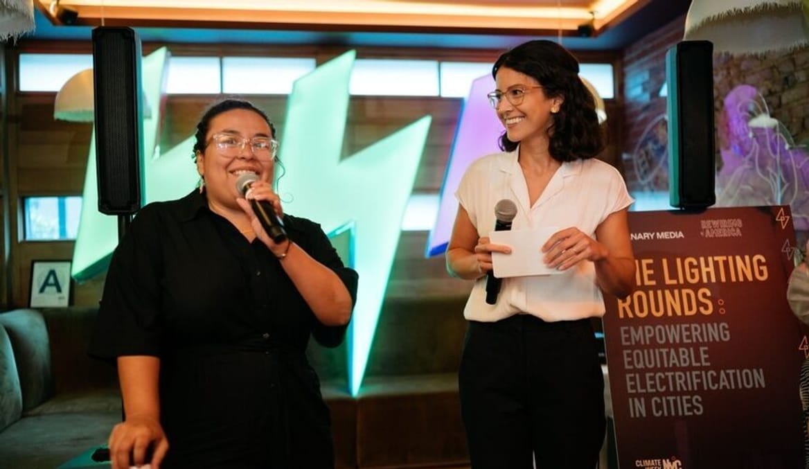 Two women speak into microphones at an event