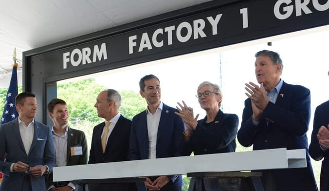 A group of people in business attire stand in an outside event tent with the words FORM FACTORY 1 over the door opening