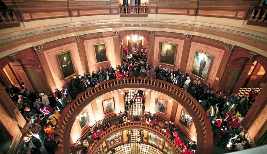 crowds of people stand near a grand multistory rotunda