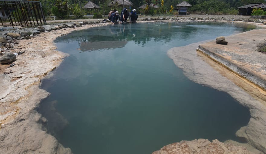 In the foreground is a small deep teal pond. Workers crouch on the far shore taking samples.