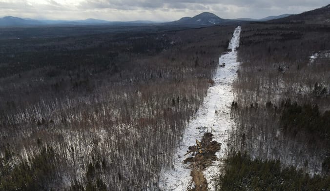 A long, snowy path in a winter forest, with mountains in the distance