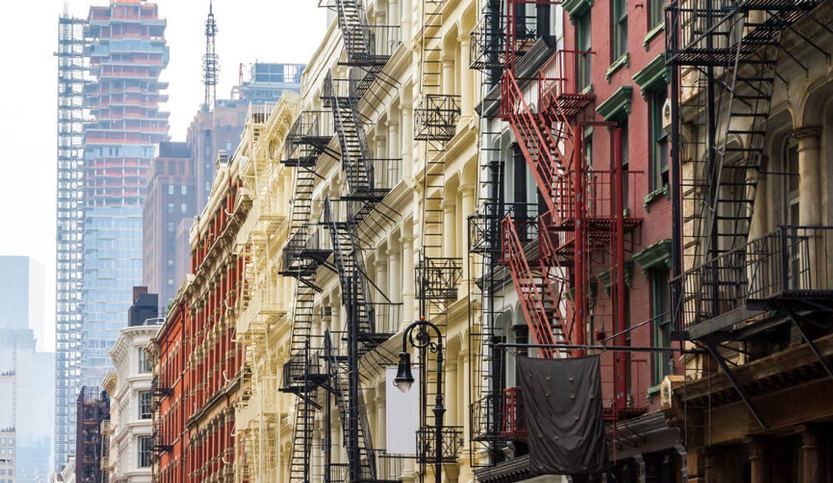 A row of colorful apartment building with black metal fire escapes. High rise buildings are seen in the background