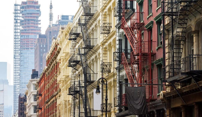 A row of colorful apartment building with black metal fire escapes. High rise buildings are seen in the background