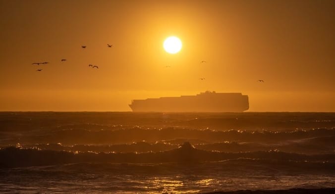 A large boat sails on the ocean under the bright orange sun
