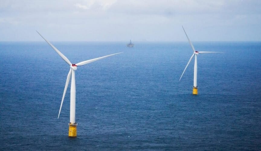Two large wind turbines in the open sea. A boat is seen in the distant background.