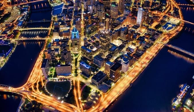 An aerial view of a city peninsula at night surrounded by water with lots of lights