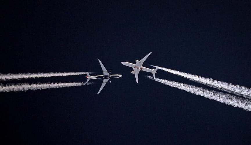 Two large planes flying in opposite directions against a dark blue sky, leaving several streams of wispy white contrails