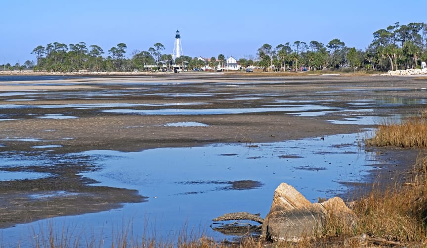 A beach with a lighthouse is seen in the distance with a shore at low tide in the foreground