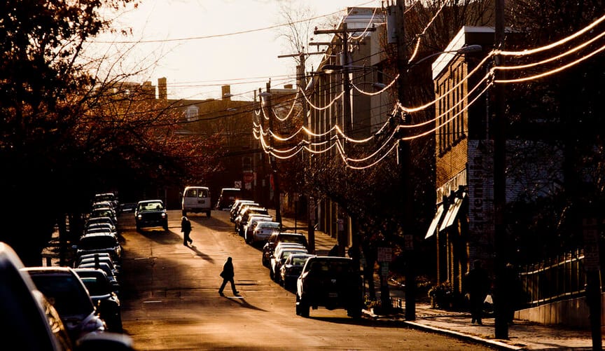 Pedestrians walk on a residential street that gently slopes uphill as the sun sets