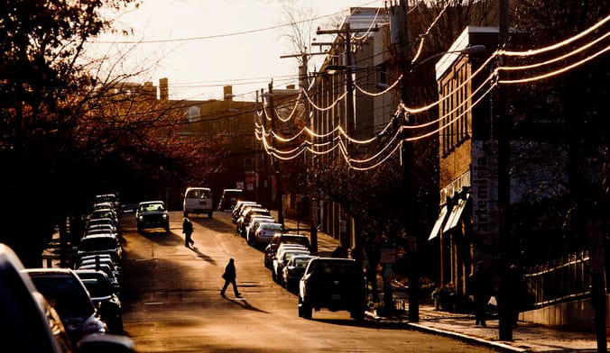 Pedestrians walk on a residential street that gently slopes uphill as the sun sets