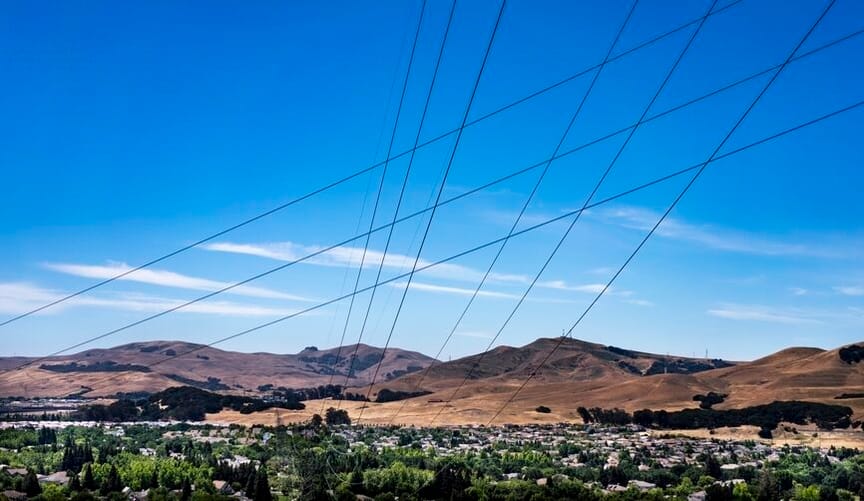 power lines criss-cross in an X formation above a tree-lined valley full of houses