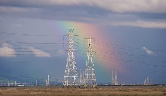 A slice of rainbow prism is seen in the sky behind large white transmission towers