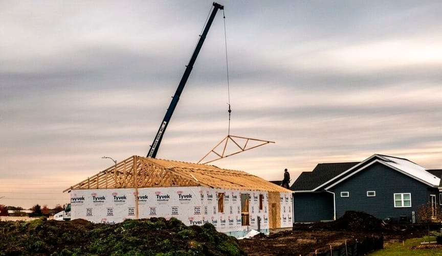 A crane installs roof framing on a residential home under construction