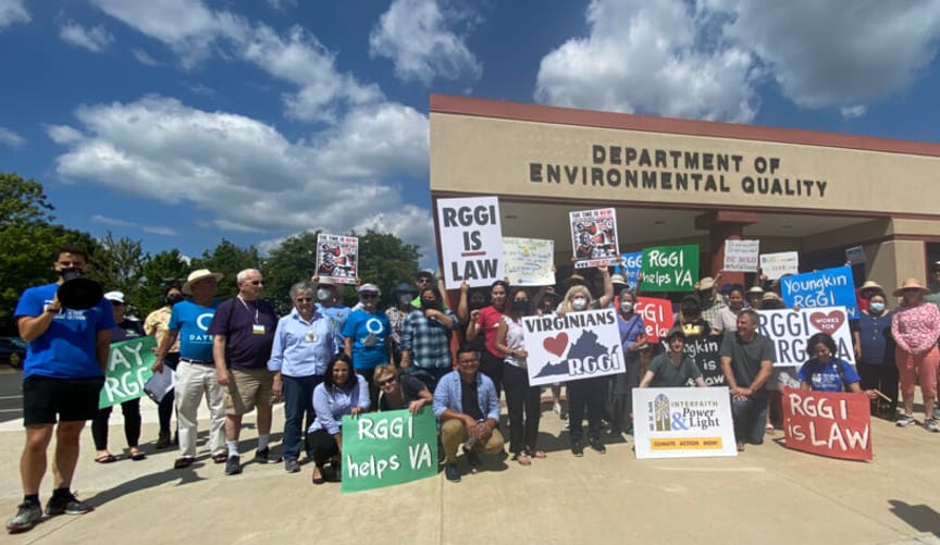 Protestors with signs supporting RGGI are gathered outside the department of environmental quality