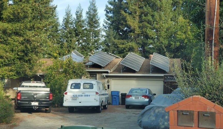 a home with rooftop solar among tall trees. Multiple vehicles are parked in the driveway.