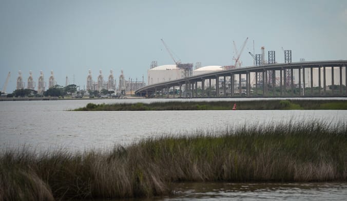 In the distance across a river and behind an arching bridge sits an enormous industrial facility