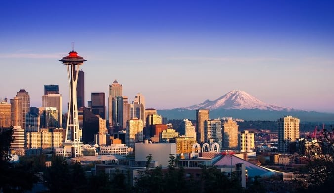 A sweeping daytime city view of downtown Seattle with Space Needle at center left and Mt. Rainier in the distance at right.