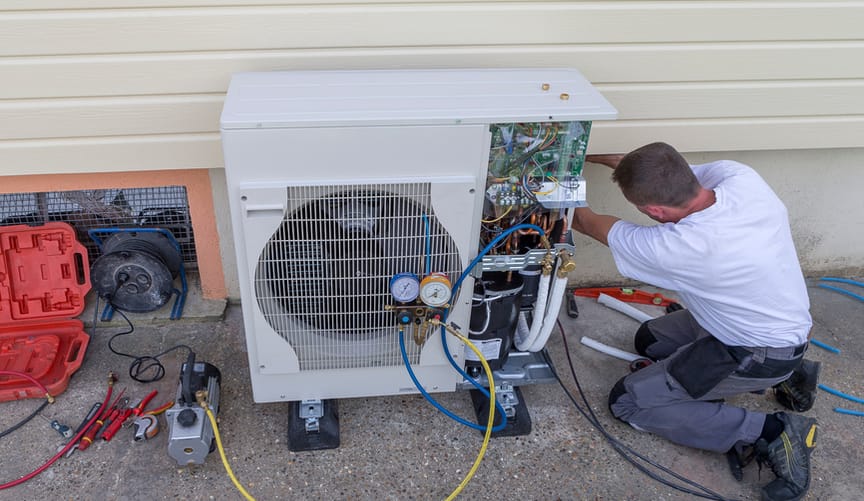 A technician works on a heat pump installed at the exterior wall of a home