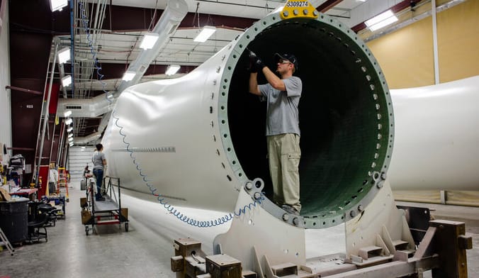A MAN USES A TOOL INSIDE A LARGE WHITE METAL CYLINDER