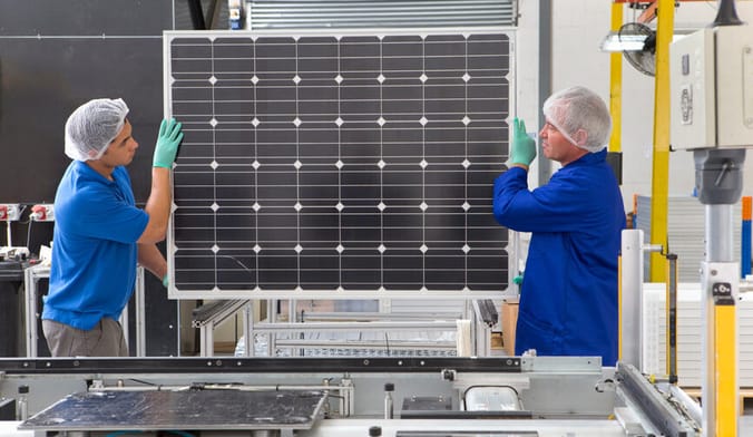 Two male factory workers lift a solar panel