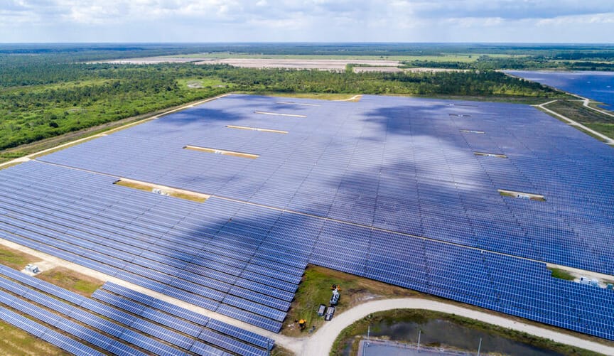 An aerial view of a large solar farm bordered by vegetation on the left side and a body of water on the right