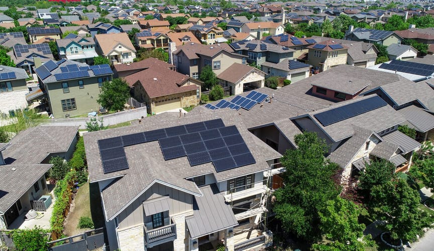 An aerial view of a neighborhood with many houses that have solar panels on their rooftop