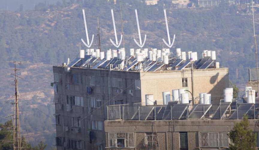 A multistory residential building with illustrated white arrows pointing at many rows of white cylindrical tanks on the roof