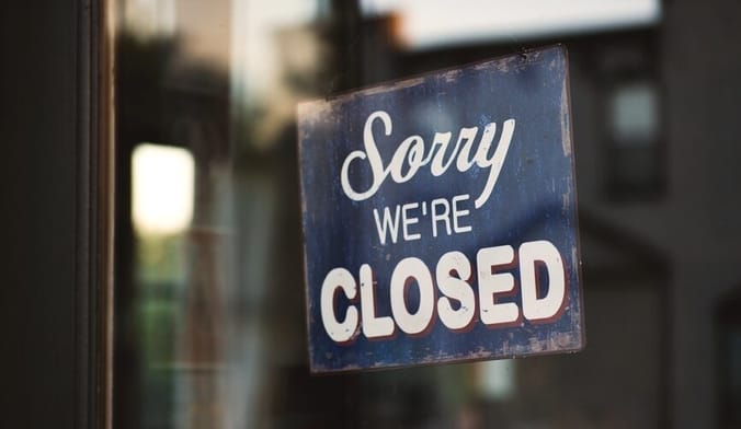 A small black sign with white lettering hangs on a glass door. It reads "Sorry we're closed"
