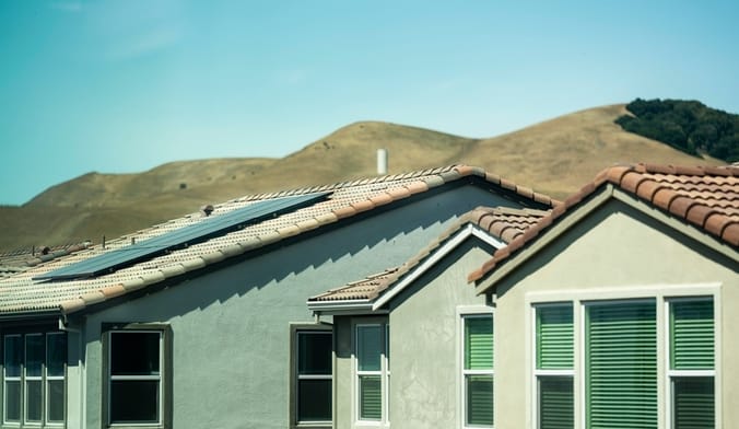 Solar panels on the red-tile roof of a stucco home, with hills in the background