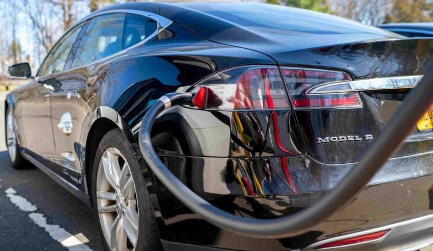 A rear view of a sleek black sedan marked MODEL S connected to an EV charger in an outdoor parking lot