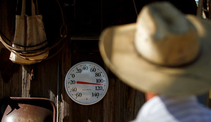 In the foreground is the back of a man wearing a large cowboy. In the background a thermometer reads 110 degrees