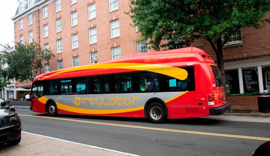 A bright red electric bus with the name circulator on the side drives down a city street