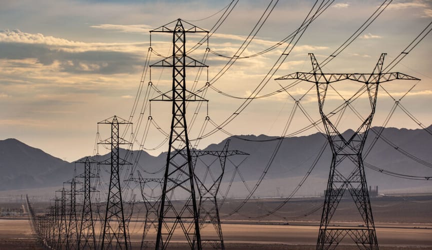 Large black transmission towers and powerlines with a mountain range visible in the distance