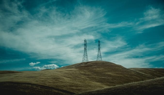 Two transmission towers stand on a green hill