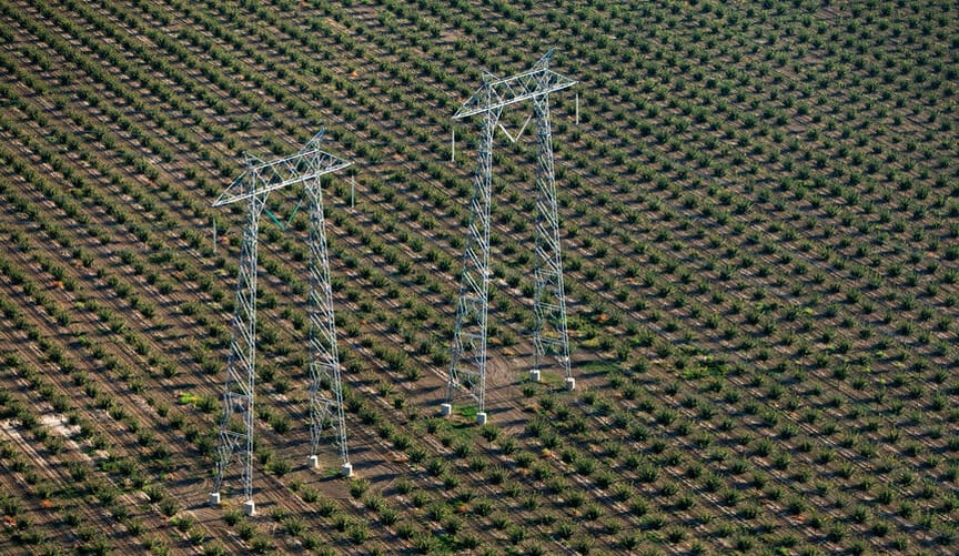 Two tall metal transmission towers stand in a vast agricultural field